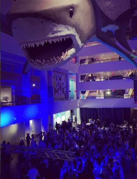 The large event space of the Natural History Museum of Balboa Park with crowd of people under large shark.